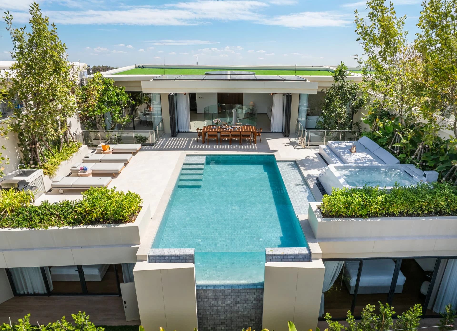 A finished Aegir villa from the air: the long pool ends in a glass wall, the living pavilion and green roof behind